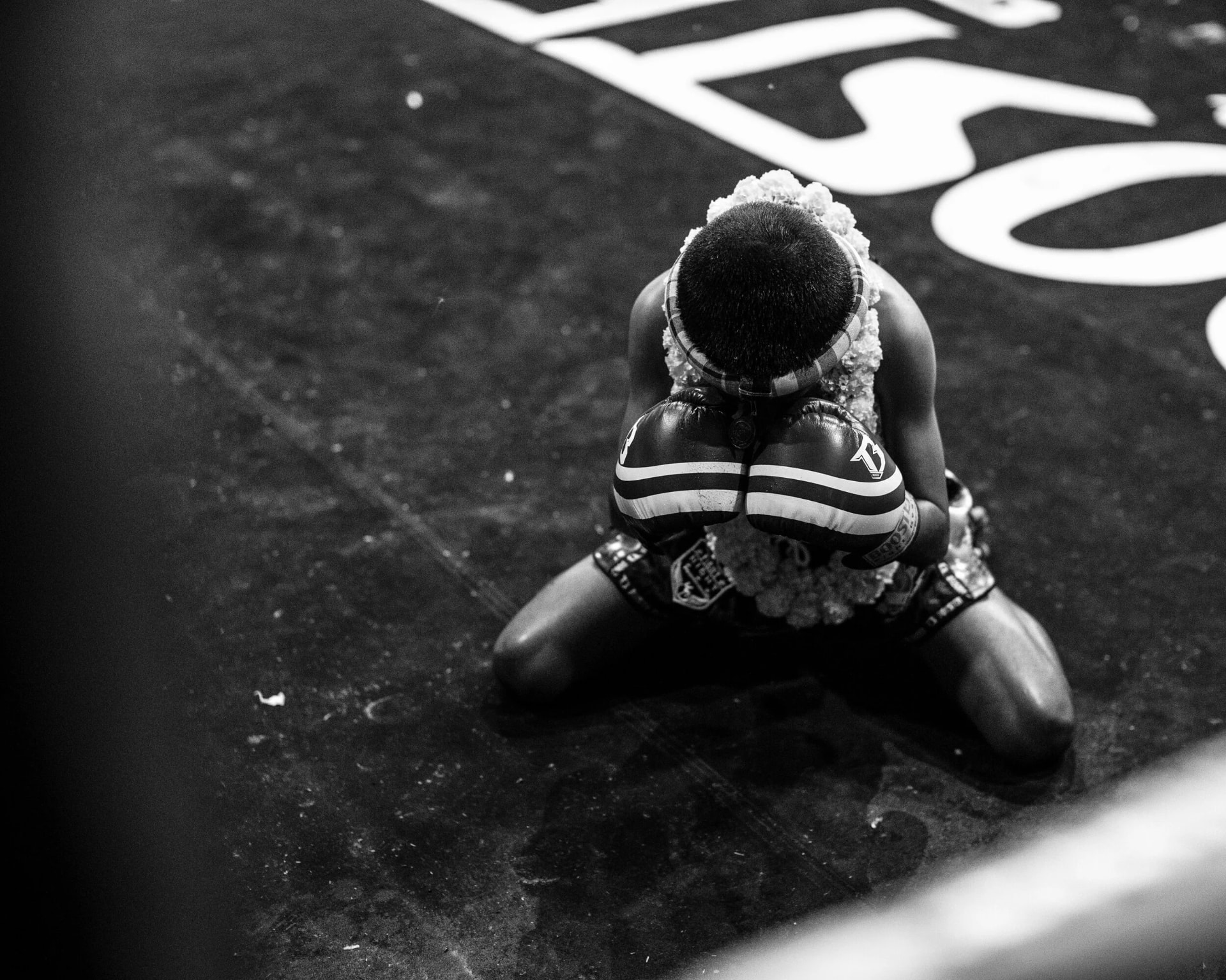 A young fighter kneeling in the ring performing the Wai Kru before a bout.