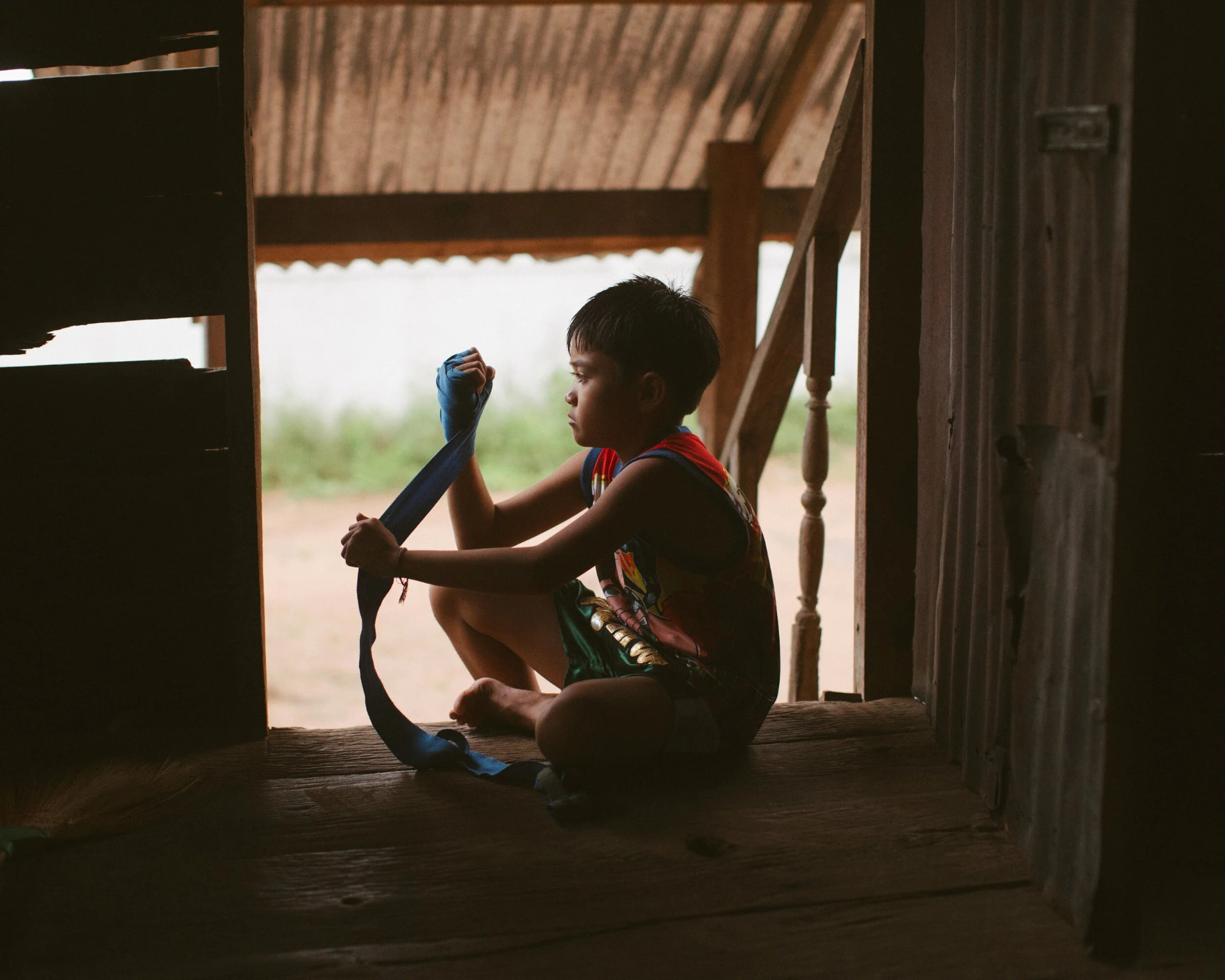 A young student sitting in a doorway wrapping his hands before training.