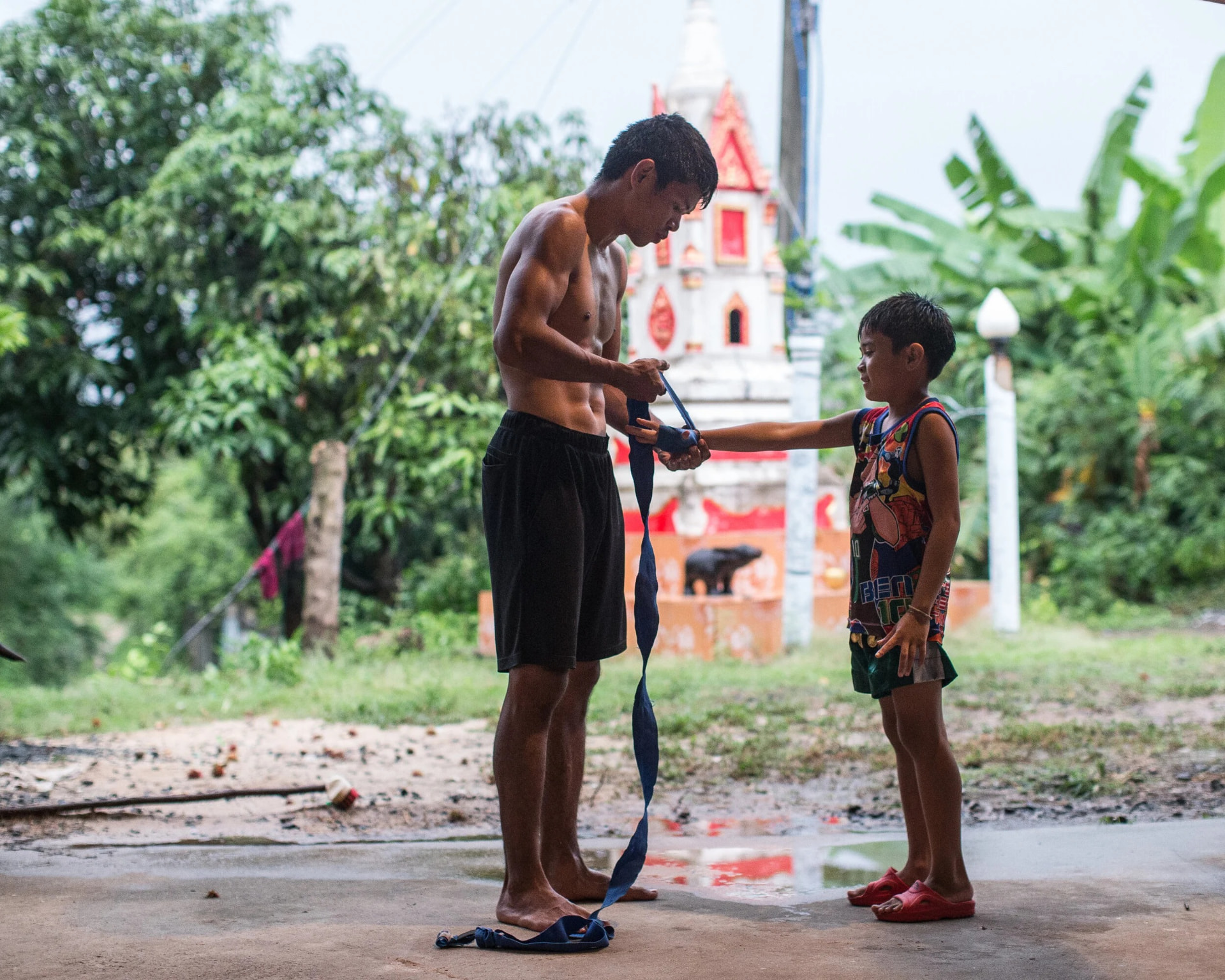 A coach passing a hand wrap to a young boy outside the gym in the village.