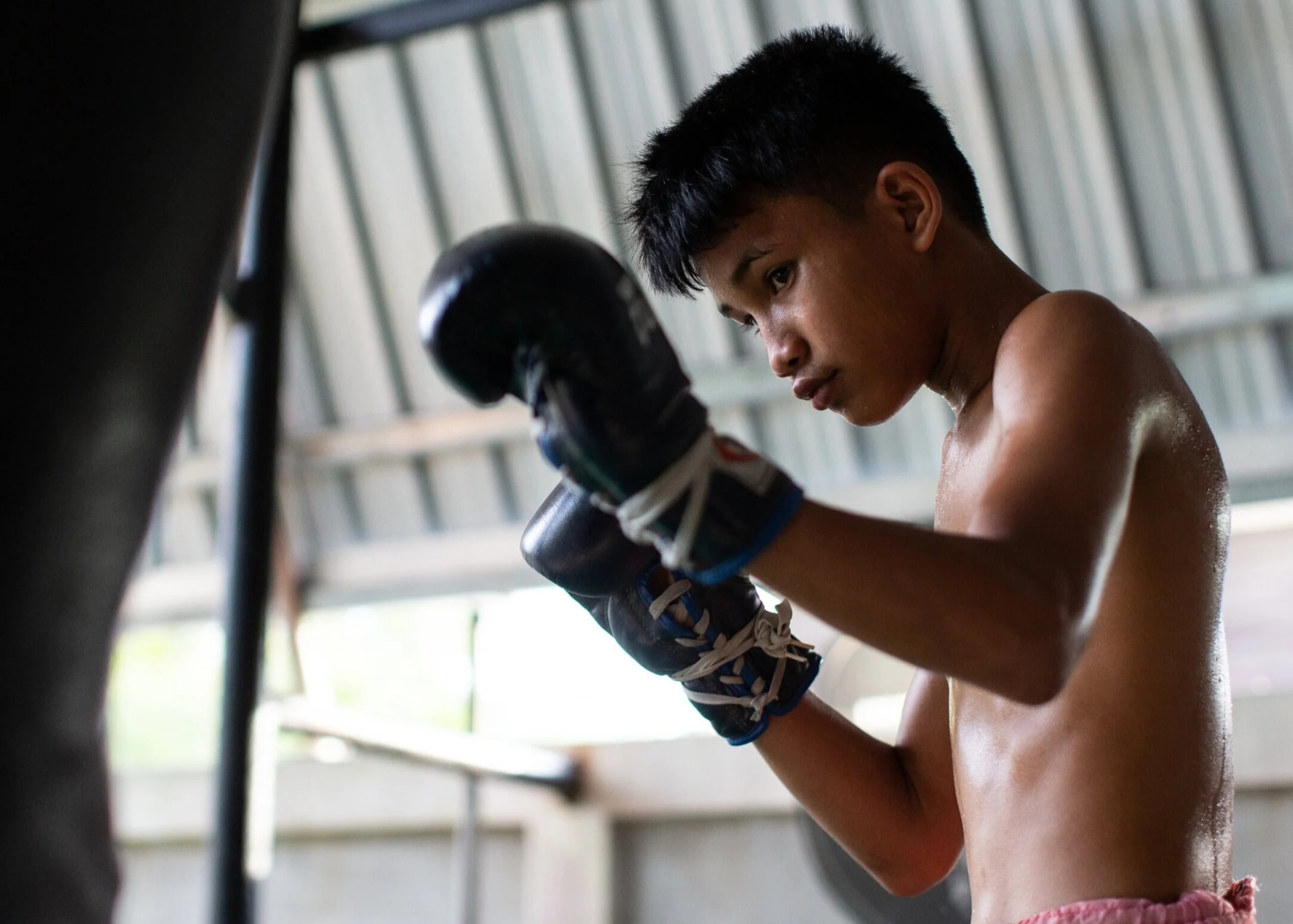 A boy in gloves working the heavy bag inside the gym.